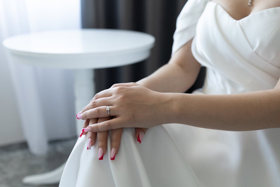 An elegant bride in a white dress showing her engagement ring and bridal manicure