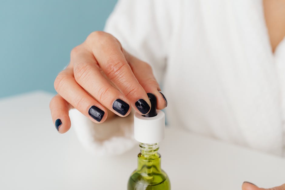 Hand holding a clear dropper bottle of cuticle oil