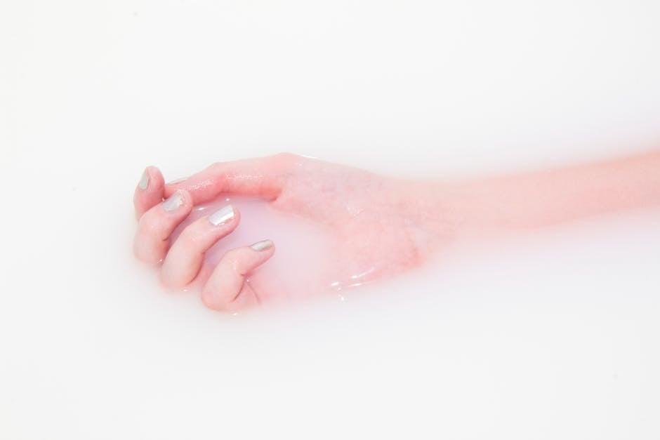 Manicured hand soaking in milky water during press-on nail removal